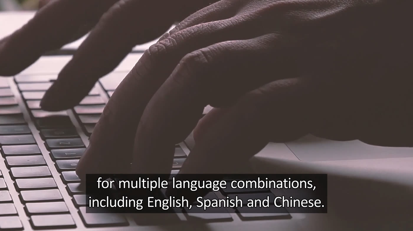 Hands typing on a laptop, with a burned-in caption reading: for multiple language combinations, including English, Spanish and Chinese.